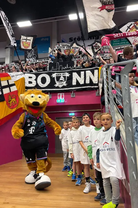 Maskottchen der Telekom Baskets Bonn neben den Einlaufkindern des VfR Flamersheim vor dem Fanblock