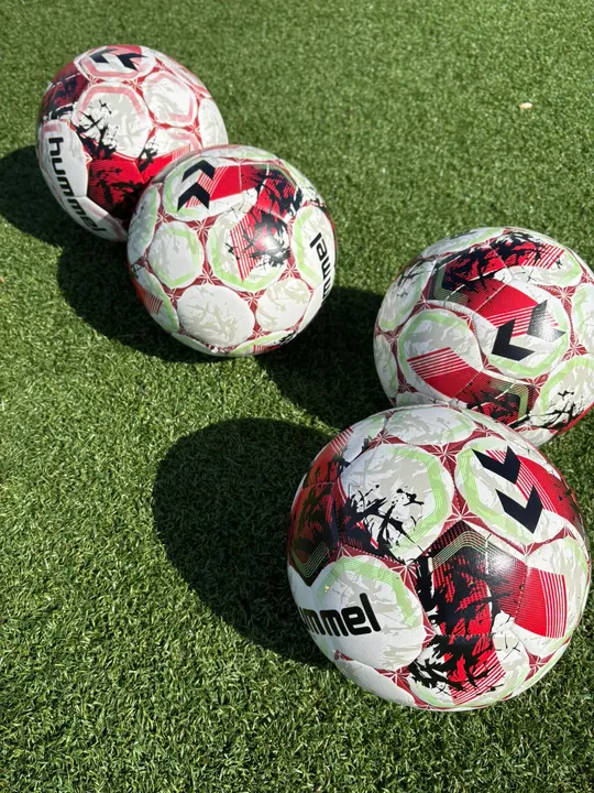 Vier Trainingsbälle liegen in der Sonne auf dem Kunstrasen