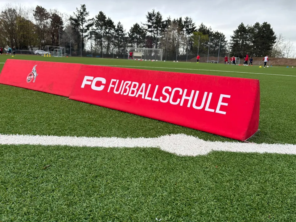 Nahaufnahme der roten Bande der FC Fußballschule auf dem Kunstrasen