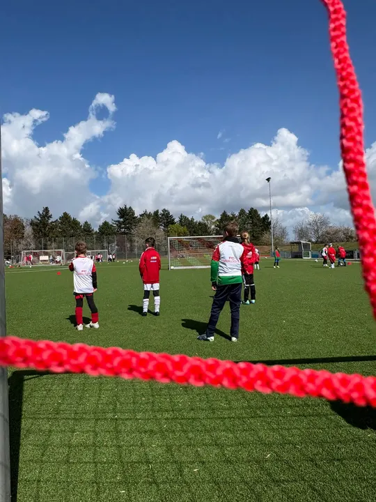 Blick durch das rote Tornetz auf Kinder in Leibchen der FC Fußballschule
