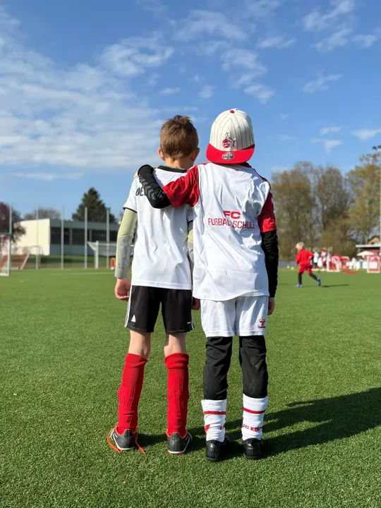Zwei Jungen stehen Arm in Arm auf dem Platz, einer mit Cap und Leibchen der FC Fußballschule