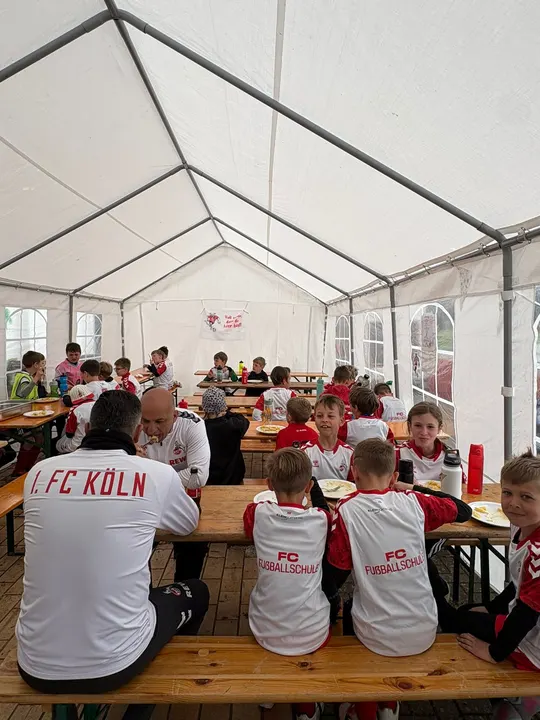 Kinder essen gemeinsam mit den Trainern an Biertischen im Zelt zu Mittag