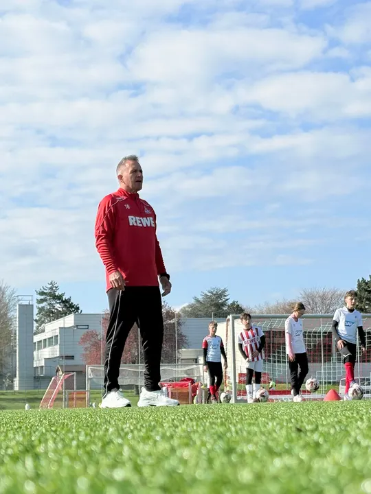 Trainer der FC Fußballschule gibt Anweisungen, dahinter warten Kinder mit Bällen