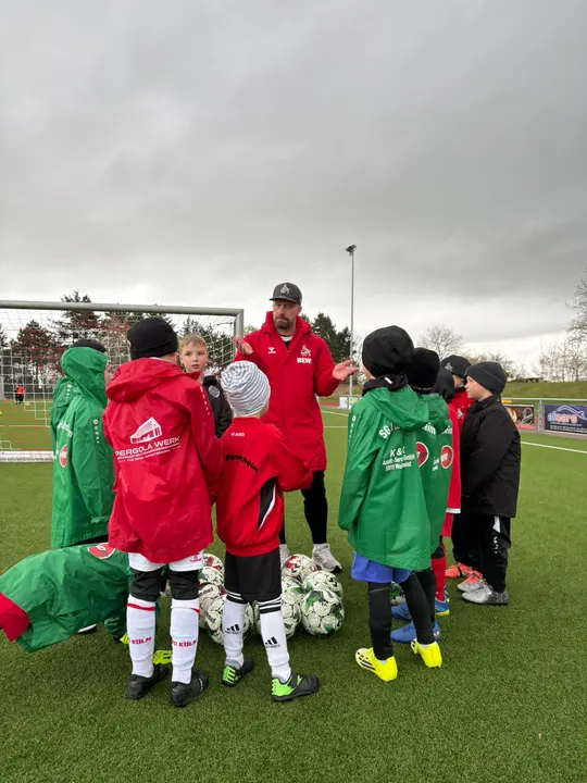 Trainer der FC Fußballschule bespricht sich mit Kindern in roten und grünen Regenjacken