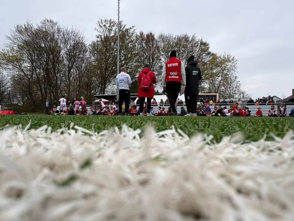 Trainerteam in Jacken von 1. FC Köln, REWE und SAP beobachtet die Kinder auf dem Platz