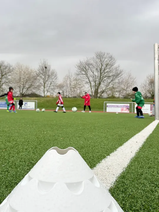 Blick über den Kunstrasenplatz mit Trainingshütchen im Vordergrund und trainierenden Kindern dahinter