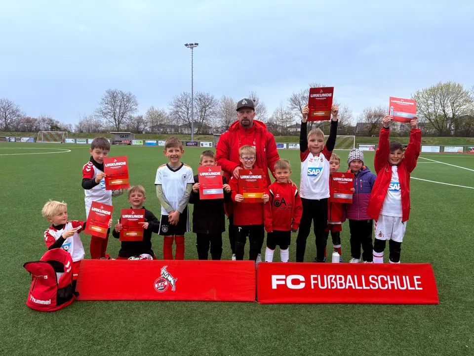 Kinder halten stolz ihre Urkunden hoch, dahinter der Trainer der FC Fußballschule