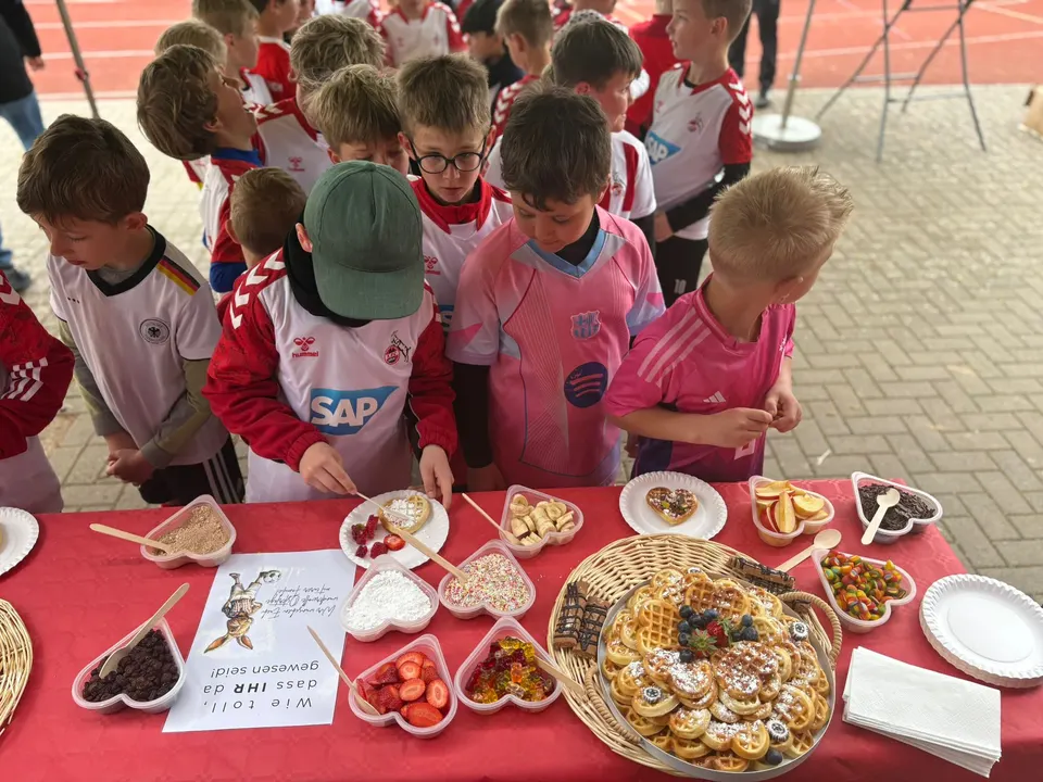 Kinder in Vereinstrikots warten an der Waffelbar auf ihre Stärkung