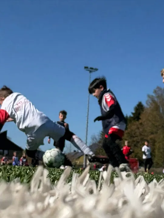 Zwei Kinder im Zweikampf um den Ball, aufgenommen aus Bodenhöhe vor blauem Himmel